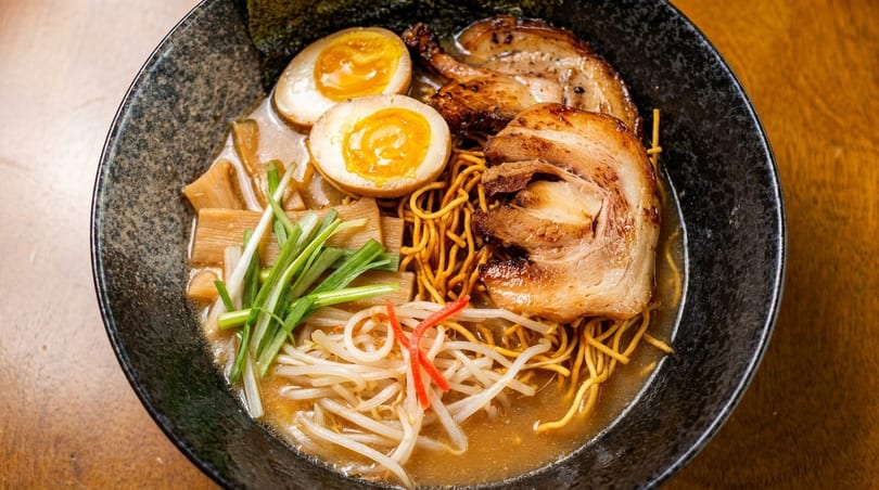 Close-up of a bowl of ramen with noodles, pork, soft-boiled eggs, bamboo shoots, and green onions.
